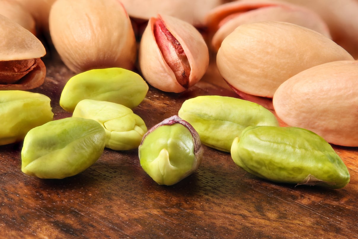 Roasted pistachios in shell, some of them peeled, green nuts visible, on wooden board. Close up macro.